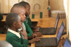 Three young boys are sitting at a table with laptops.