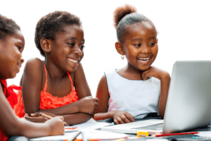 Two young girls sitting at a table with a laptop.